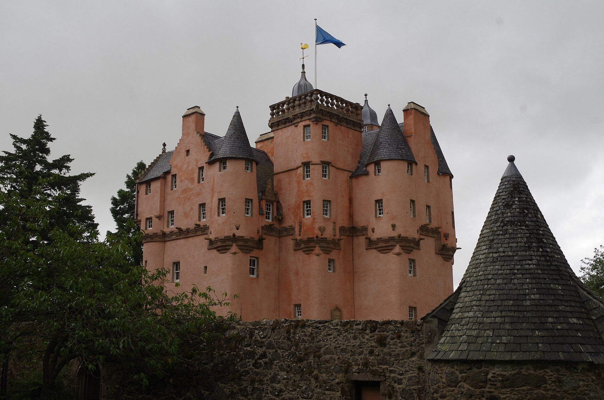 The pink harled tower of Craigievar Castle against a grey sky, a conical roof in front.